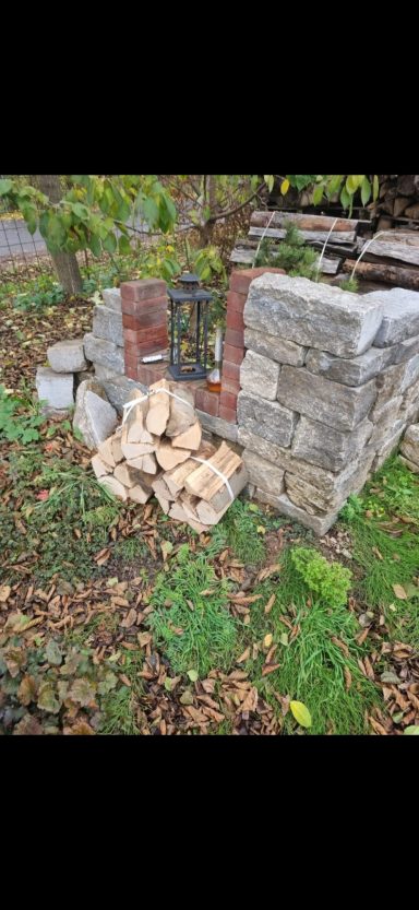 Stapel aus trockenem Brennholz neben Steinmauer im Garten 
